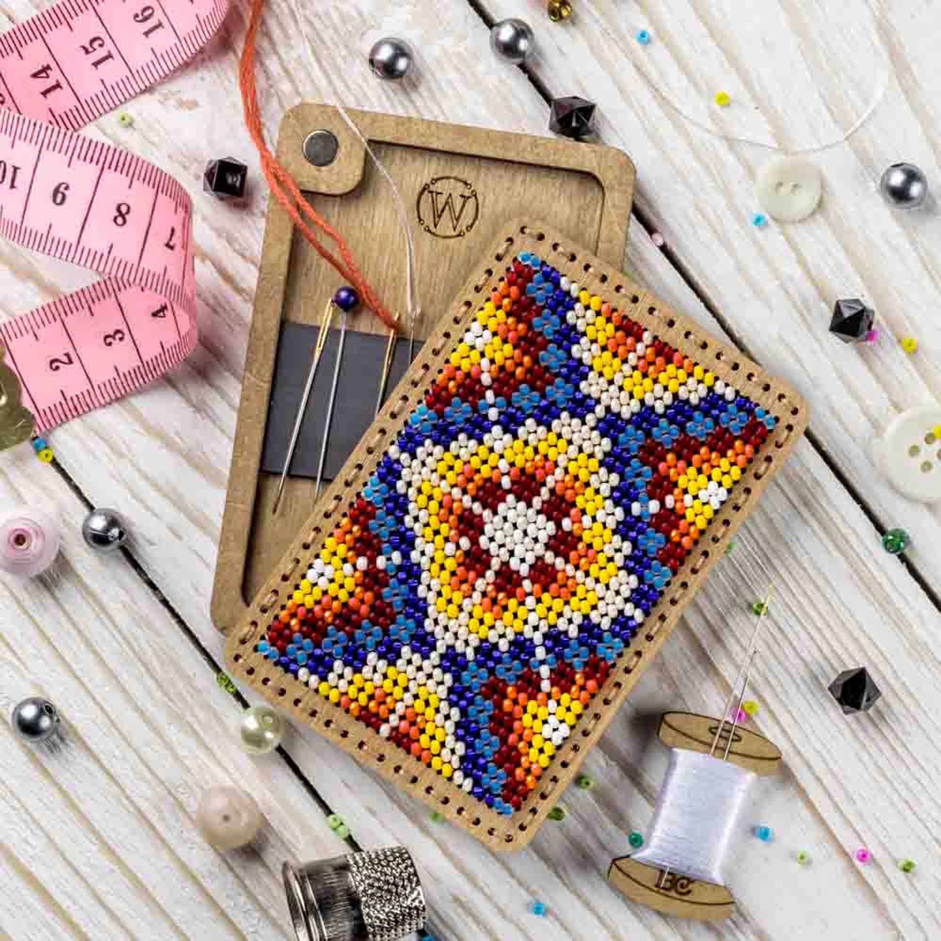a piece of beaded art next to a sewing needle